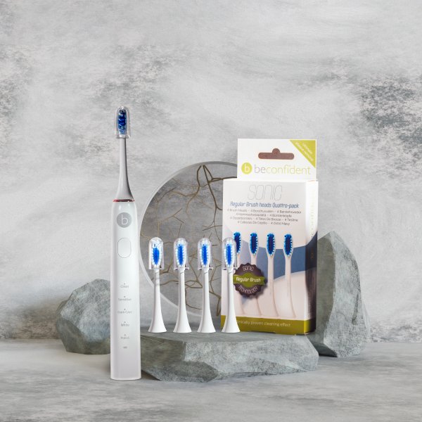 Beconfident white/rosegold sonic whitening electrical toothbrush next to four regular white brush heads and Beconfident regular brush heads quattro-pack in front of stone background