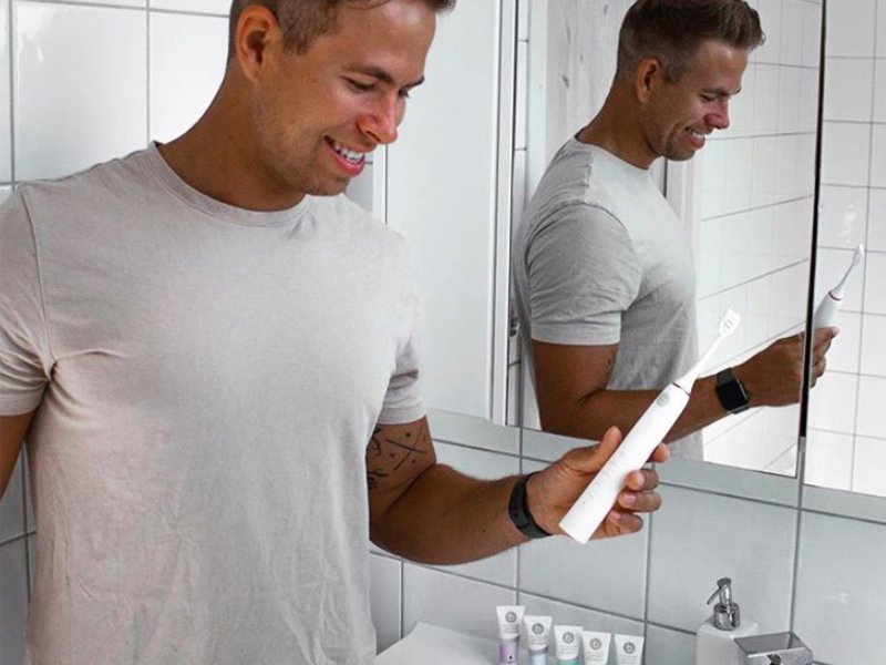 Guy in bathroom with beconfident silver sonic whitening toothbrush and 5x75ml Beconfident multifunctional whitening toothpaste